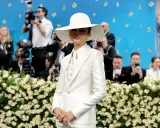 Zendaya, deslumbrante con traje blanco y sombrero, posa ante cámaras y flores.