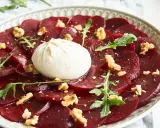 Rote Bete Carpaccio mit Burrata, Walnüssen und Rucola auf einem Teller.