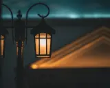 Ciepłe światło zabytkowych lamp miejskich rozświetla zmierzch, rzucając geometryczne cienie na budynek.