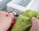 Odkręcanie odpowietrznika grzejnika, gdy jest zimny na dole. Woda kapie na zieloną ściereczkę.