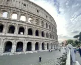 Le Colisée, monument emblématique de Rome, se dresse majestueusement sous un ciel nuageux. Des visiteurs explorent ses environs pavés.