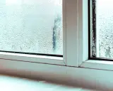Krople deszczu na zaparowanym oknie plastikowym. Woda skrapla się na szybie, tworząc małe kropelki i smugi.