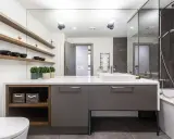 Moderno baño con ducha, bañera y lavabo sobre mueble gris. Estanterías de madera con cuencos negros. Un ejemplo de presupuesto de reforma de baño.