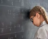Mädchen mit Brille lehnt frustriert am Tafelbild mit Matheaufgaben. Die note 5 in der schule ist zu viel.