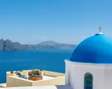Blaue Kuppel einer Kirche in Oia, Santorini, mit Blick auf das tiefblaue Meer und die zerklüftete Küste.