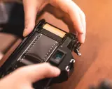 Manos insertando rollo de película en cámara analógica, un paso clave para aprender como revelar fotos en casa.