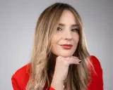 Francesca Florio, con un blazer rosso, appoggia il mento sulla mano, un sorriso pensieroso.