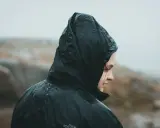 Person i regnkläder med huvan uppdragen, droppar på tyget. Vattenpelare 10000 klarar detta väder.