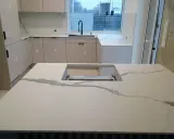 Nowoczesna kuchnia z wyspą i blatem z białego spieku kamiennego, imitującego marmur.