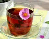 Ein Glas Cistus Tee mit einer rosa Blüte. Die Cistus Tee Wirkung ist bekannt für ihre entzündungshemmenden Eigenschaften.