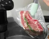 Ein Steak mit Rosmarin und Gewürzen wird für das Suvid Garen in einen Vakuumbeutel gelegt.