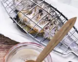 Ein ganzer Fisch liegt in einem Grillkorb, bereit zum Fisch grillen auf dem Elektrogrill. Kräuter und Zitronenscheiben sind im Fisch.