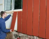 Man monterar en röd träpanel på en fasad. En dropplist syns under fönstret.