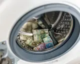 Stosy polskich banknotów w pralce, sugerujące pranie pieniędzy.