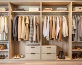 Interior de armario empotrado con ropa colgada y doblada, y zapatos en estantes.