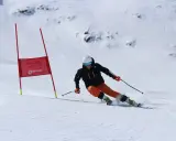 Narciarka na trasie slalomu, w kasku i goglach, dynamicznie pokonuje zakręt, wzbijając śnieg.