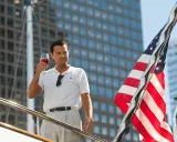 Leonardo DiCaprio z kieliszkiem wina na jachcie, obok amerykańska flaga i wieżowce.