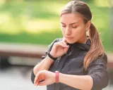 Kobieta w czarnej kurtce sprawdza na zegarku swój niski puls po treningu.
