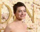 Emma Stone sorride, con un trucco che esalta i colori che stanno bene alle castane con pelle chiara. Lo sfondo è un muro di rose rosa e bianche.