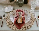 Une table dressée avec élégance, une assiette fleurie, une serviette bordeaux et une **fourchette à la française** en cuivre, prête pour un repas raffiné.