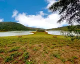 Prato verde con tavoli da picnic affacciati sul **lago di Canterno**, circondato da dolci colline sotto un cielo azzurro con nuvole bianche.