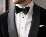 A man wears a sharp black suit with a crisp white shirt and a black bow tie, ready for a formal occasion.