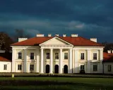 Pałac w Siedlcach, jedna z głównych atrakcji miasta, z charakterystycznym portykiem i czerwonym dachem, na tle burzowego nieba.