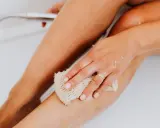 Une main utilise un gant de toilette pour exfolier sa peau, révélant une peau douce et lisse. C'est une étape clé pour savoir comment exfolier sa peau.