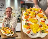 En glad man håller upp en vacker påsktårta i långpanna, dekorerad med grädde, jordgubbar, aprikoser och gula blommor.