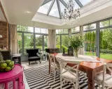 Une élégante veranda couloir avec un lustre, une table en bois et des fauteuils, donnant sur un jardin verdoyant.