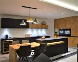 Une cuisine moderne aux accents beige et noir, avec un îlot central, des meubles en bois et des suspensions colorées.
