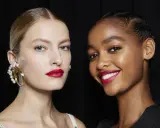 Dos modelos lucen un maquillaje para boda con labios rojos vibrantes y piel radiante. Una lleva un pendiente de perlas, la otra sonríe.