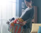 Ciężarna kobieta z koszem prania. Dźwiganie w ciąży bywa wyzwaniem, ale ona radzi sobie z codziennymi obowiązkami.