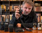 Mężczyzna prezentuje sprzęt CB radio, pokazując różne modele i akcesoria, które wpływają na zasięg.