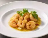 Saftige, gebackene Garnelen mit Knoblauch und Petersilie auf einem weißen Teller.