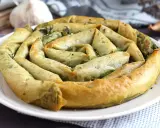 En gyllene, spiralformad burek med spenatfyllning, perfekt för ett hemlagat burek recept. Vitlök och lök i bakgrunden.