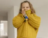 Ein fröhliches kleines Mädchen im gelben Pullover hält Schlüssel in der Hand. Die Frage "ab wann Kinder alleine lassen" beschäftigt Eltern oft, doch dieses Bild strahlt Unbeschwertheit aus.