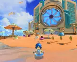 Astro playroom na plaży. Robot w kółku do pływania, monety i urocze stworki na piasku. W tle futurystyczny budynek z wielkim niebieskim wentylatorem.