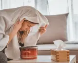 Une femme apprend comment faire une inhalation, la tête couverte d'une serviette au-dessus d'une casserole de vapeur.