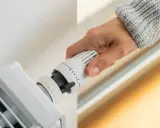 Dłoń reguluje termostat grzejnika. Zastanawiasz się, ile kosztuje wymiana termostatu?