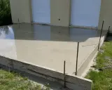 Une nouvelle dalle béton fraîchement coulée, prête à sécher. Les coffrages en bois et les fers à béton délimitent la zone.