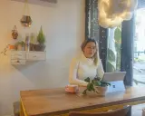 Kobieta pracuje na laptopie w kawiarni, ciesząc się kawą i roślinami. To idealne miejsce na dodatkową pracę zdalną.