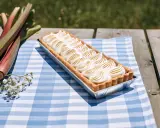 Tarte à la rhubarbe meringuée alsacienne, prête à être dégustée sur une nappe à carreaux bleus.