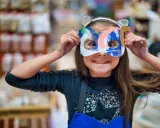 Une jeune fille, le visage caché par un masque coloré, explore la symbolique du visage et la joie de la transformation.