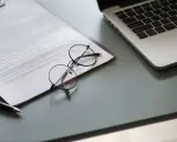 Okulary na dokumencie z tekstem, obok laptopa. Dokument może zawierać pełnomocnictwo lub strategię marketingową.