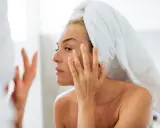 Une femme, serviette sur la tête, applique une crème sur son visage. Un geste essentiel pour prendre soin de sa peau en hiver.