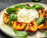 Burrata z grillowanymi brzoskwiniami, bazylią i orzeszkami piniowymi na talerzu.