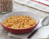 Un plato humeante de pasta e ceci, con garbanzos y macarrones en una salsa rojiza, junto a un tarro de garbanzos secos.