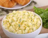 Pyszna sałatka z jajkiem, idealna na śniadanie lub lunch. Podana w białej misce, obok świeżych liści sałaty i chrupiących croissantów.