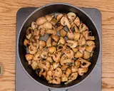 Champiñones al ajillo dorándose en una sartén, con perejil picado en un cuenco al lado.